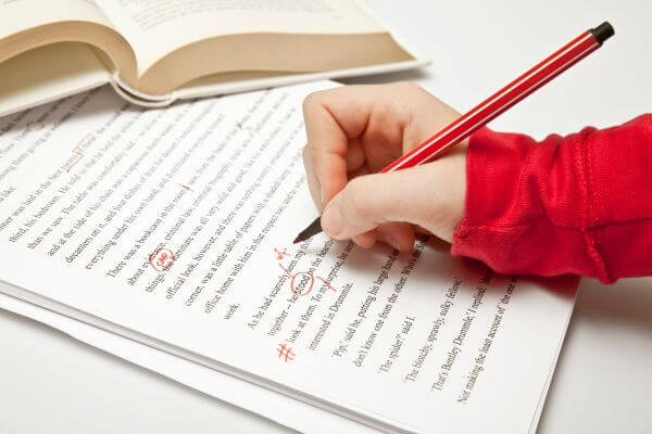 Image of a girl's hand in a red sleeve holding a pen while doing  a script revision or proofreading.