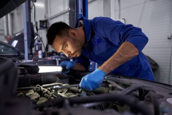 Image of a mechanic fixing some parts of the car, wearing his blue uniform and gloves. 