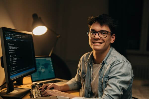 Image of a man wearing an eyeglass in a denim jacket, working on his computer.