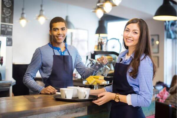 Image of a man and woman working together in a coffee shop wearing the same apron.