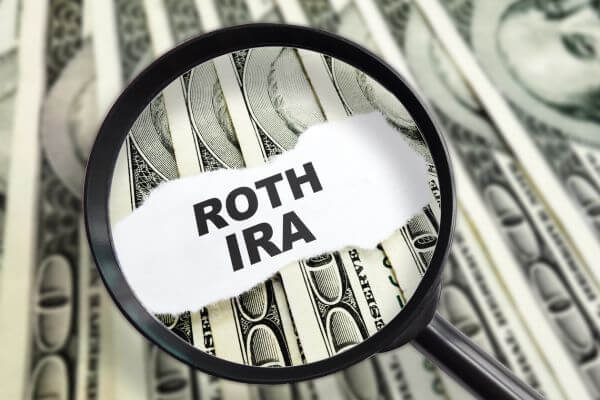 Image of a magnifying glass and a text of Roth IRA together with dollar money behind.