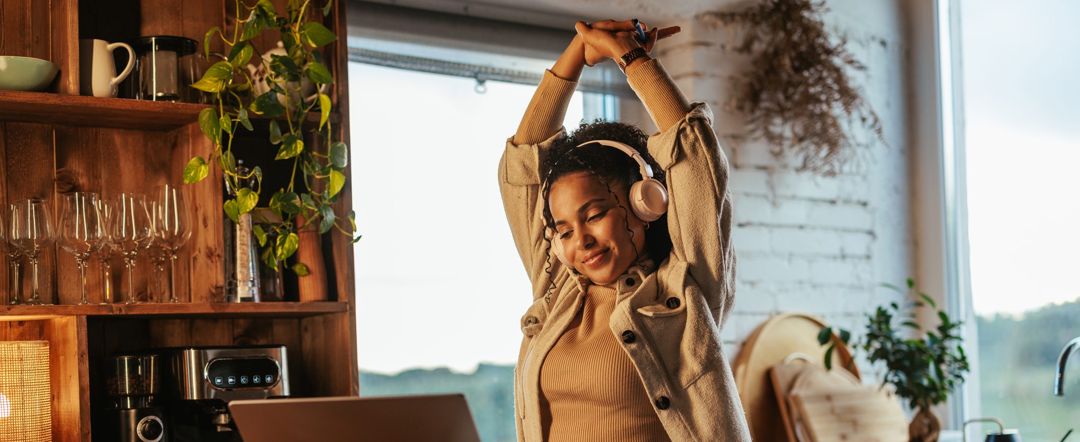 While working at a laptop computer, a woman wearing headphones stretches her arms over her head.