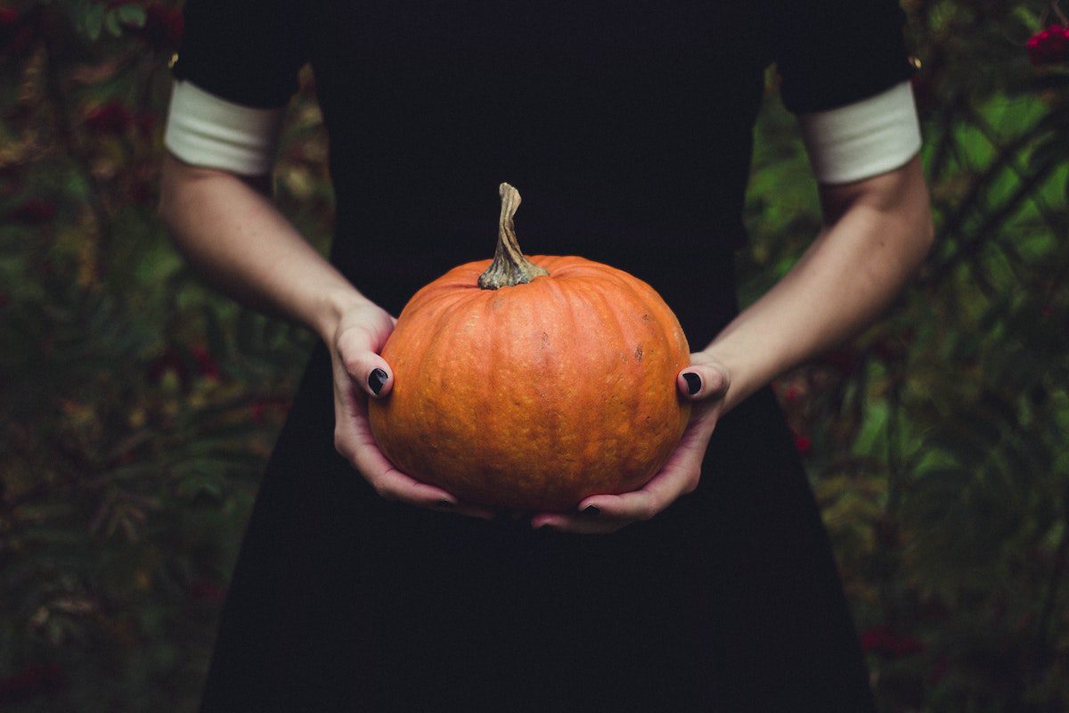 Creepy woman holding a pumpkin near a haunted house